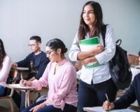 Leerlingen werken in een klas terwijl een student met boeken binnenkomt