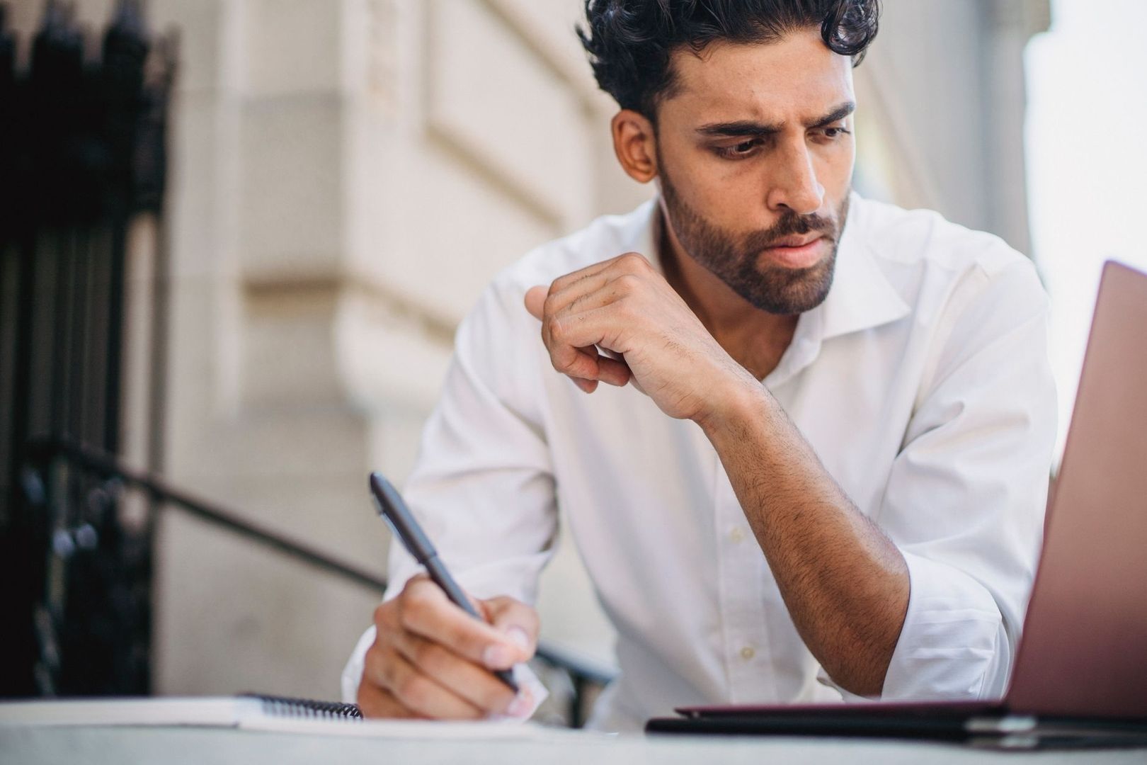 Gefocuste man maakt aantekeningen naast een laptop